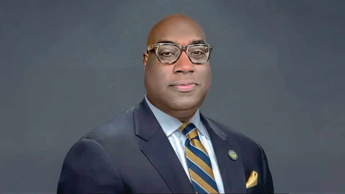 A man with dark skin wearing a suit, tie and glasses