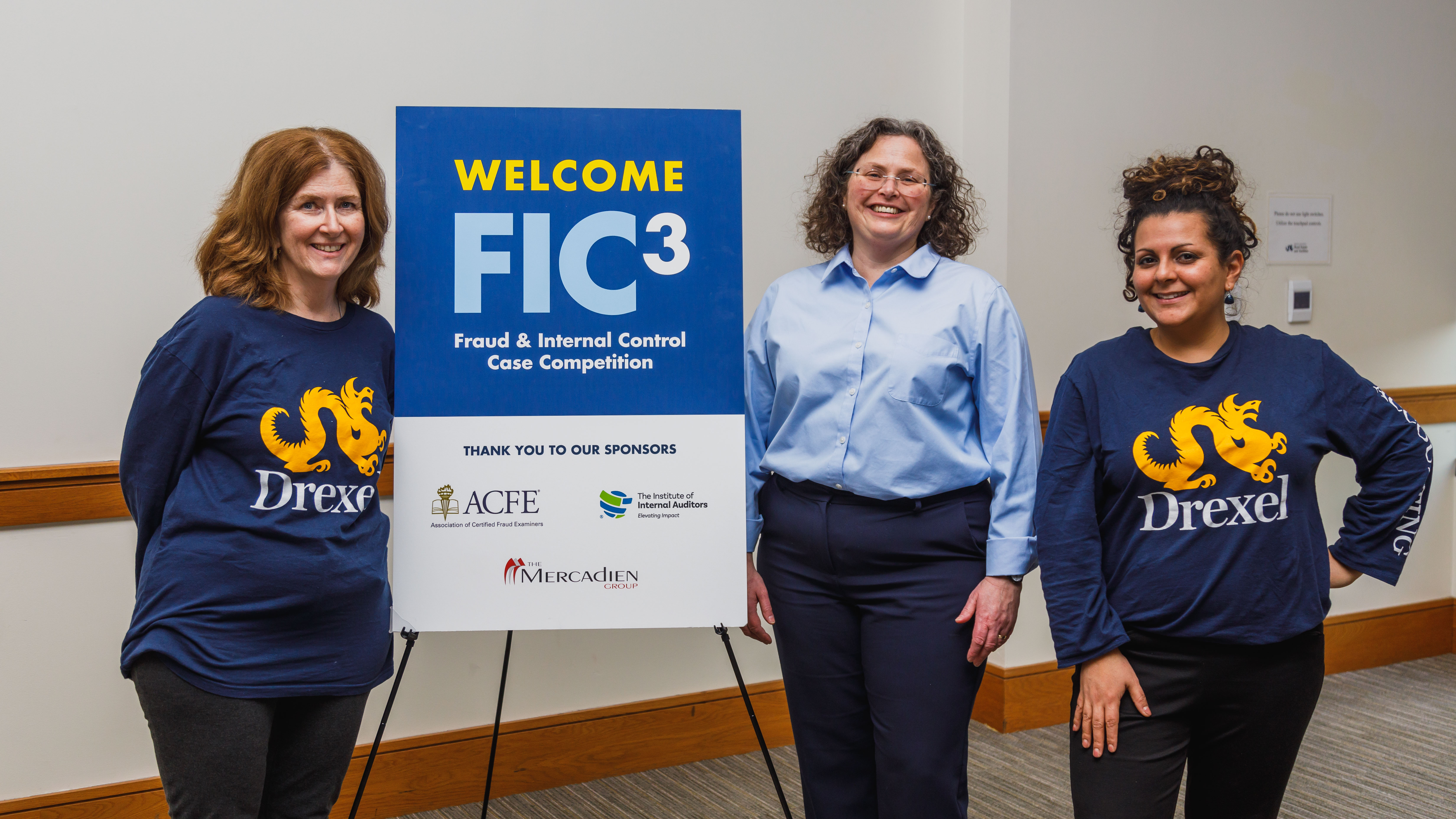 Two women on the left and right wearing navy Drexel University t-shirts and one woman at center wearing a light blue dress shirt