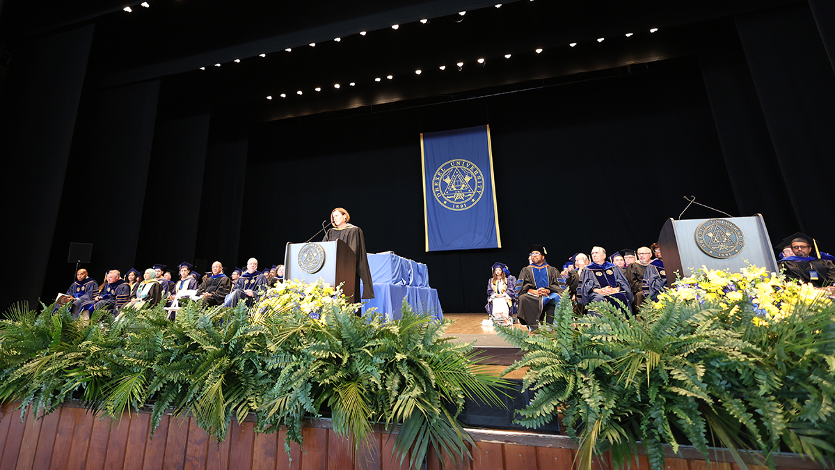 The stage at the Mann Center for the Performing Arts, with a female speaker at the podium and people dressed in academic robes visible in the background