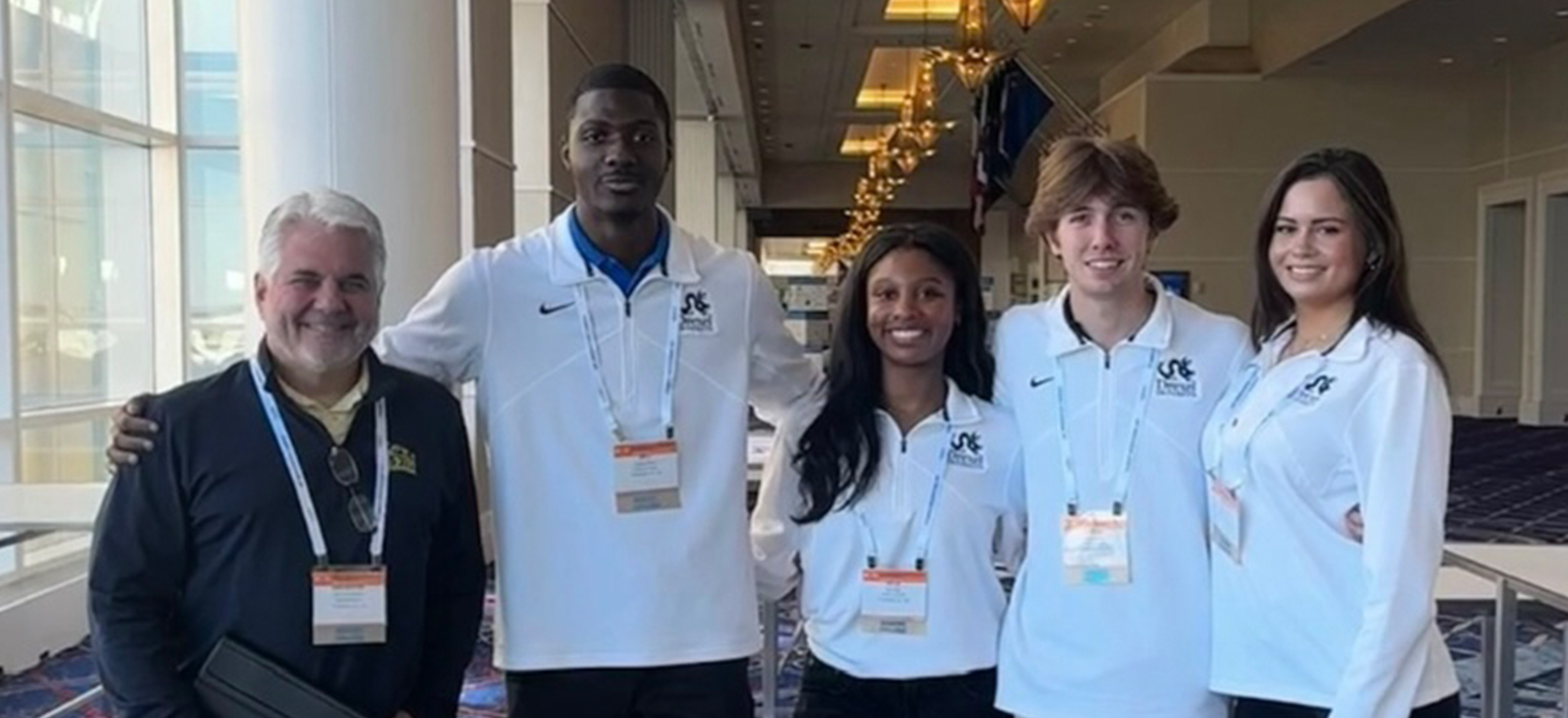 Five individuals, with one on the far left wearing a navy jacket and the other four wearing white shirts with the Drexel University logo visible