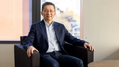 Headshot of Dali Ma, PhD Department Head & Associate Professor of Management sitting in chair in front of window