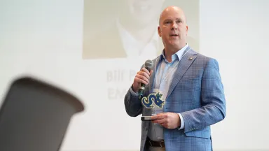 Man wearing a blue suit jacket holding a transparent award with a navy Drexel logo on it