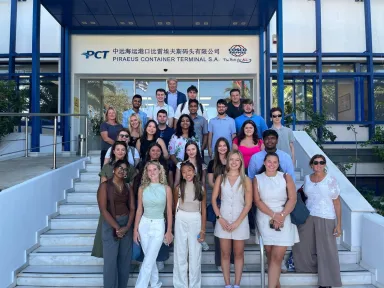 Students in business casual dress standing in six rows on stairs. The title Piraeus Container Terminal S.A. and some Chinese characters are visible in the background.